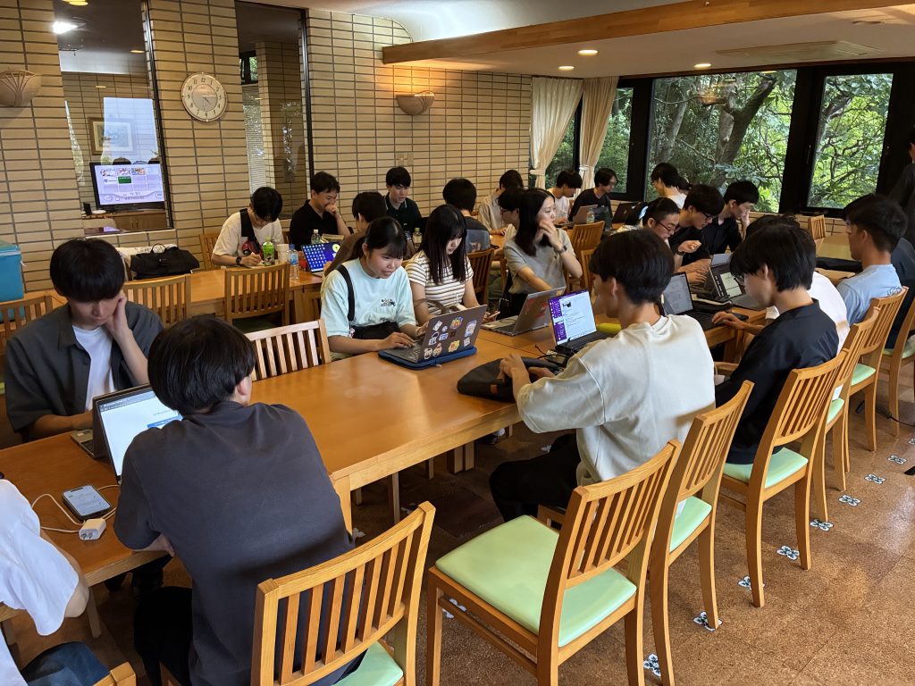 室内でパソコンを使い，グループでデータ分析に取り組む学生たち